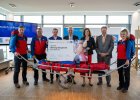 Gruppenfoto u.a. mit Herrmann und Bergwachtlern in Uniform mit plakativem Spendenscheck und Rettungstrage der Bergwacht