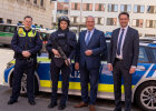 Innenminister Joachim Herrmann und Justizminister Georg Eisenreich neben Polizist und Polizistin in Schutzkleidung vor Polizeiauto