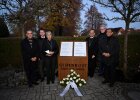 Kirchner und weitere Teilnehmerinnen und Teilnehmer neben Gedenktafel mit Kränzen