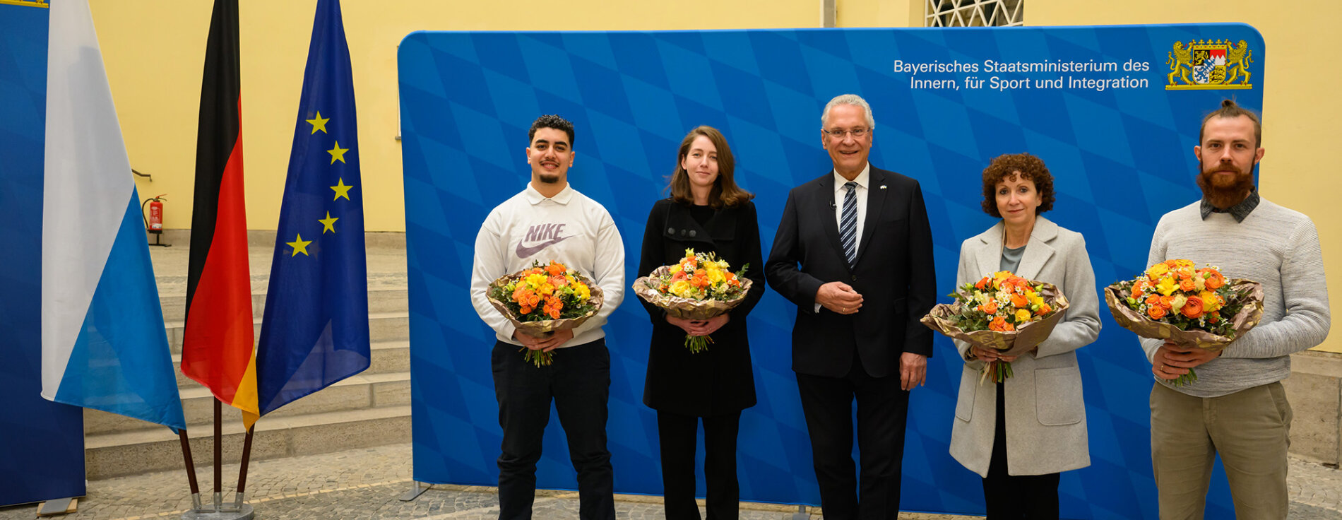 Gruppenfoto mit Innenminister Joachim Herrmann und den vier Eingebürgerten mit Blumensträußen