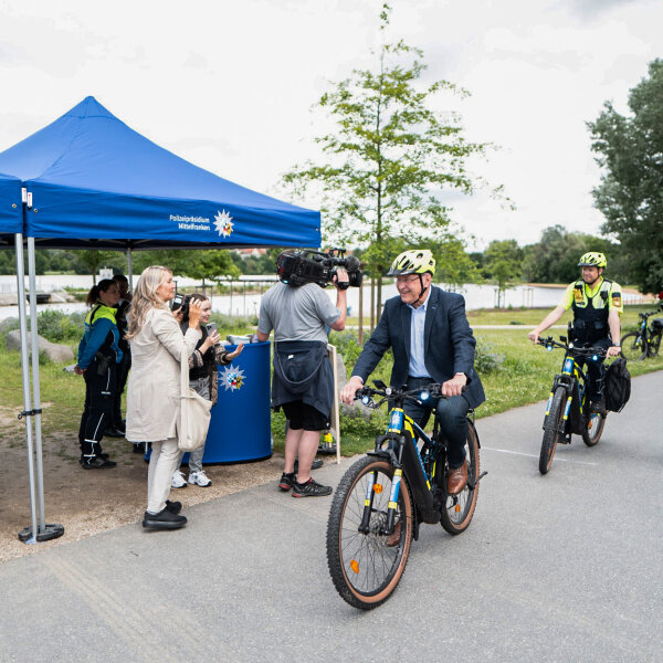 Innenminister Joachim Herrmann fährt auf einem Polizeifahrrad am Polizeikontrollstand vorbei