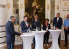 Kirchner mit Mikrofon an Stehtischen mit weiteren Diskussionsteilnehmern
