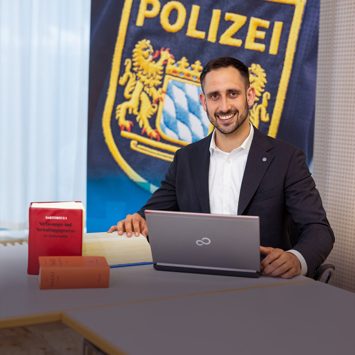 Polizeijurist vor Polizei-Rollup mit Laptop und Gesetzesbänden