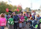 Viele Schulkinder von hinten, zwei Feuerwehrleute verteilen Rucksackcover